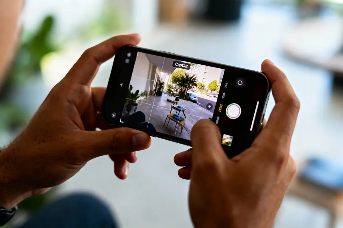 Personne utilisant un smartphone pour photographier une terrasse avec table en bois, à l'extérieur, utilisant l'application CapCut.