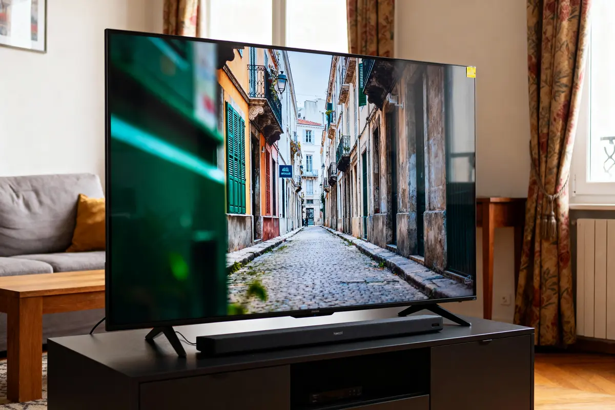 Télévision montrant une ruelle pavée, entourée de bâtiments anciens, dans un salon confortable et lumineux.
