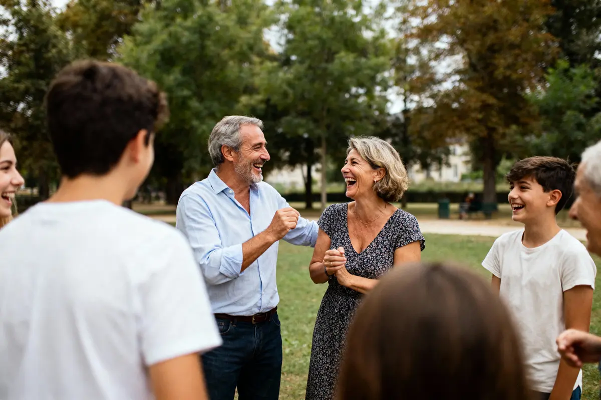 Groupe de personnes souriantes discutant joyeusement dans un parc verdoyant. Arrière-plan avec arbres. Moment convivial.