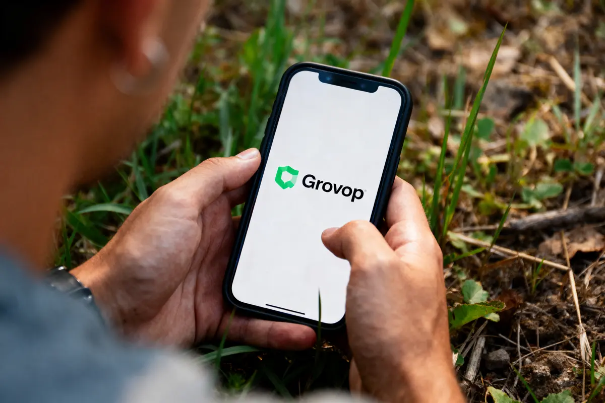 Personne tenant un smartphone affichant le logo "Grovop" sur fond blanc, assise dans l'herbe.