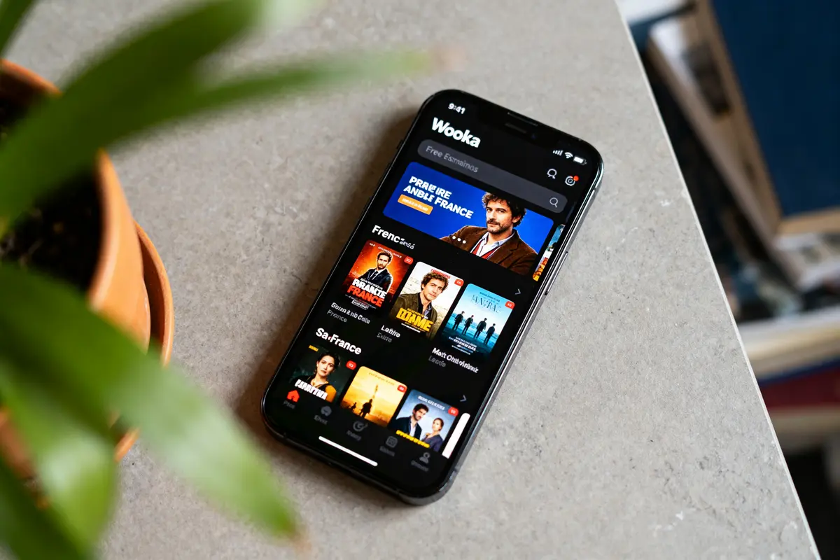 Smartphone affichant l'application Wooka avec des films et séries variés sur fond de table